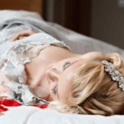 Dornröschenschlaf. Eine junge Frau liegt auf einem Bett , von Rosenblütenblättern umgeben, und schläft.