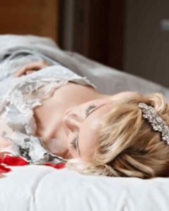 Dornröschenschlaf. Eine junge Frau liegt auf einem Bett , von Rosenblütenblättern umgeben, und schläft.