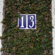 Bedeutung der Zahl 13: Eine Hausnummer 13. Blaues Schild mit weißer Schrift an einem Haus.