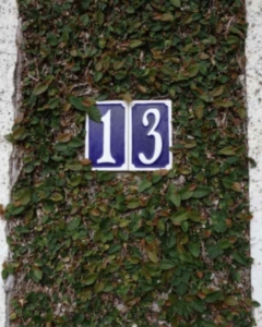 Bedeutung der Zahl 13: Eine Hausnummer 13. Blaues Schild mit weißer Schrift an einem Haus.